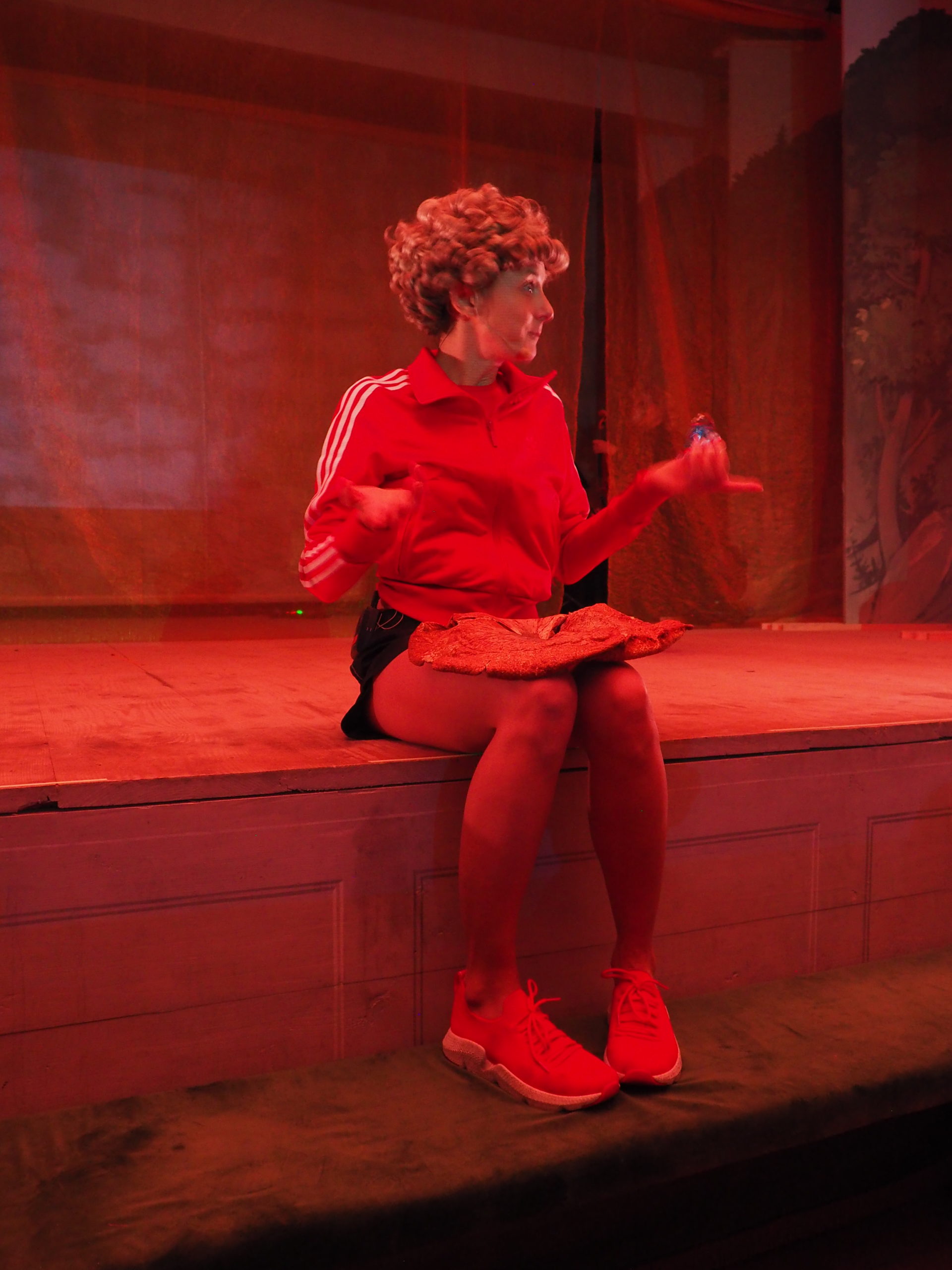 Artystka siedzi na skraju sceny i trzyma na kolanach grzyba