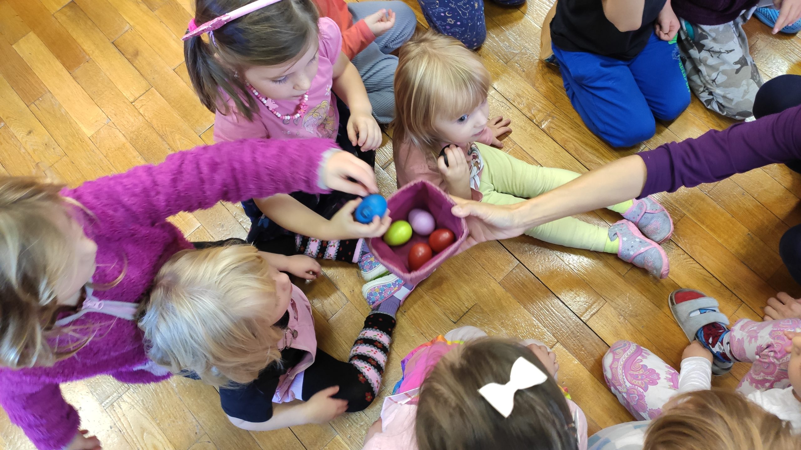 Dzieci siedzą na podłodze i wyjmują instrumenty z koszyczka