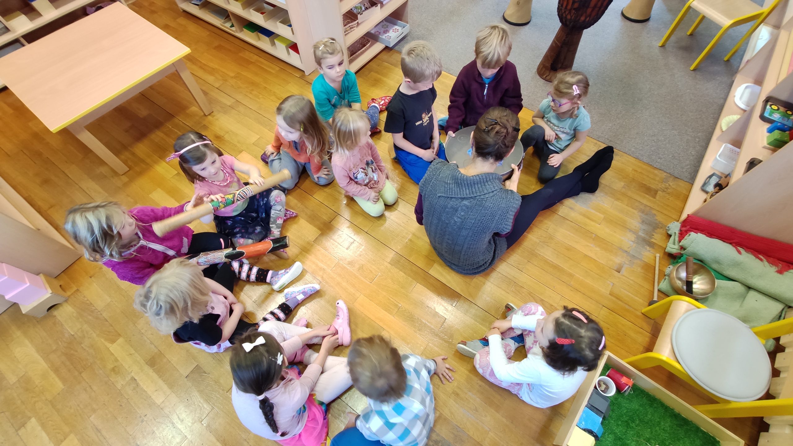 Dzieci siedzą w kołku na podłodze, na środku siedzi instruktorka i pokazuje im bęben oceaniczny
