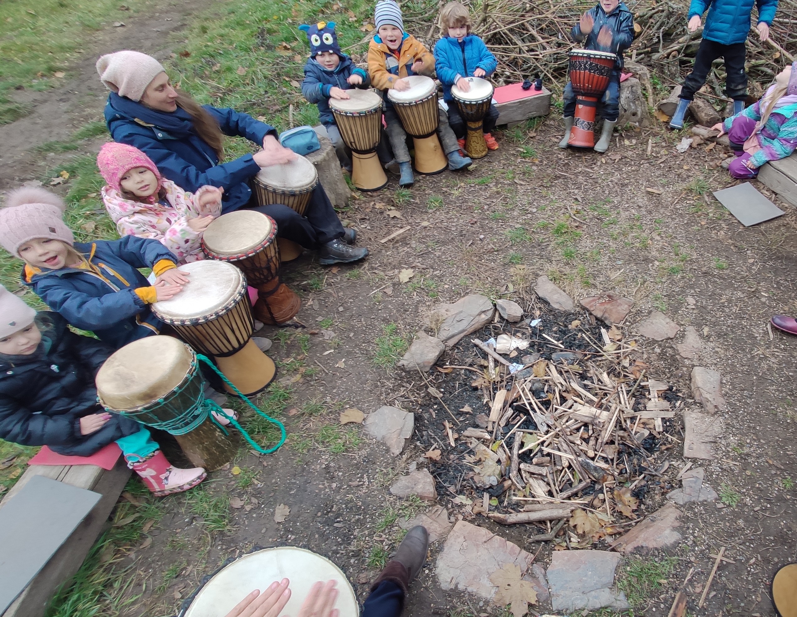 Dzieci siedzą w kole wokół miejsca na ognisko i grają na bębnach