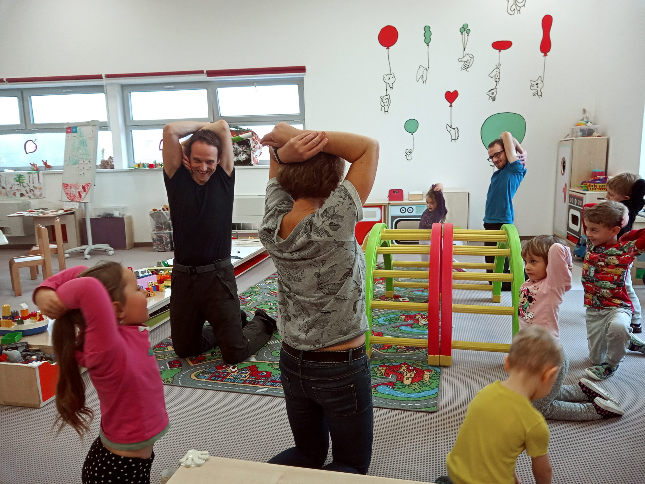 Dzieci naśladują instruktora i stoją zakładając ręce za głowę